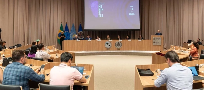 Uma sala de conferências ampla com várias pessoas sentadas ao redor de mesas retangulares