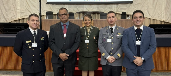 Cinco pessoas vestindo uniformes da Marinha e do Exército. Ao fundo, uma bancada e um telão. Eles pousam para foto.