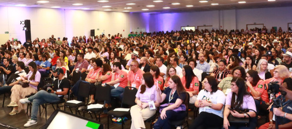 Pessoa em pé no palco de um auditório falando para o público