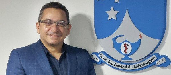 Pessoa de pé na frente da logo do Cofen