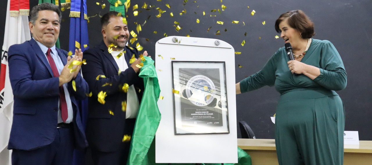 Três pessoas em pé e uma placa simbolizando um selo entregue pelo Cofen às instituições de saúde
