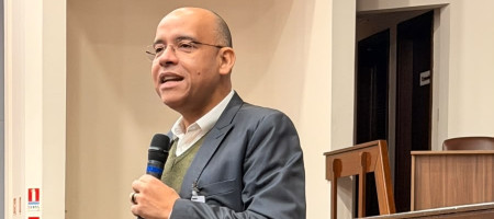 Pessoa em pé falando ao microfone para uma plateia
