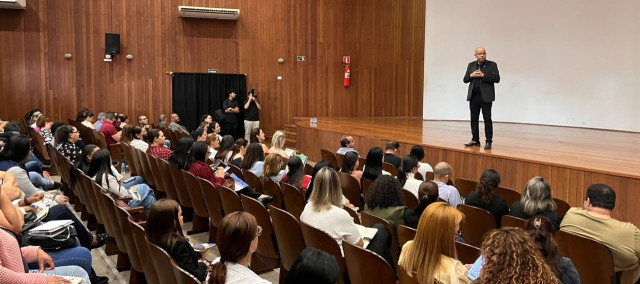 Uma pessoa em pé num auditório falando para as pessoas que estão sentadas